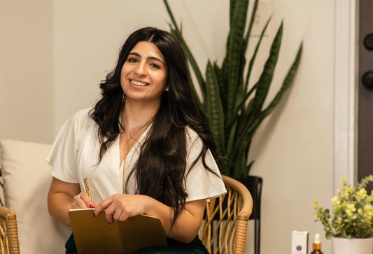 Woman brand founder sitting in a chair with notebook smiling.