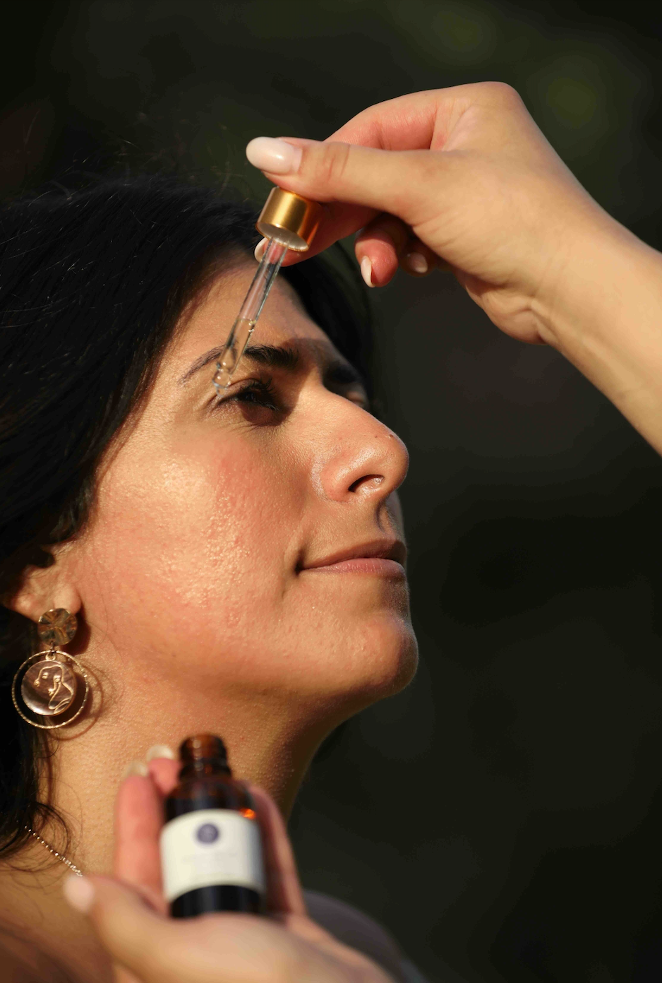 Woman using dropper to apply facial oil to face 